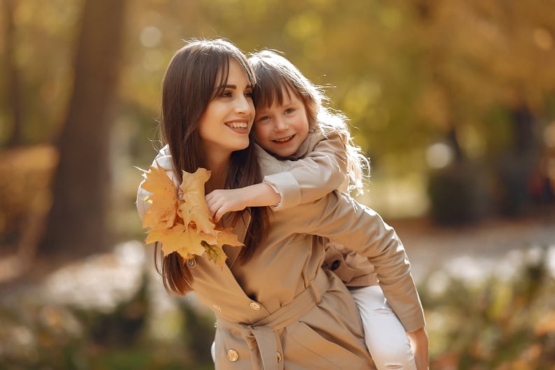 Happy mother giving daughter piggyback ride in park